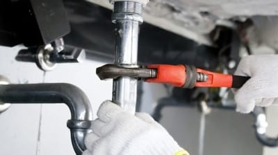 Plumber using a wrench to tighten a pipe connection under a sink