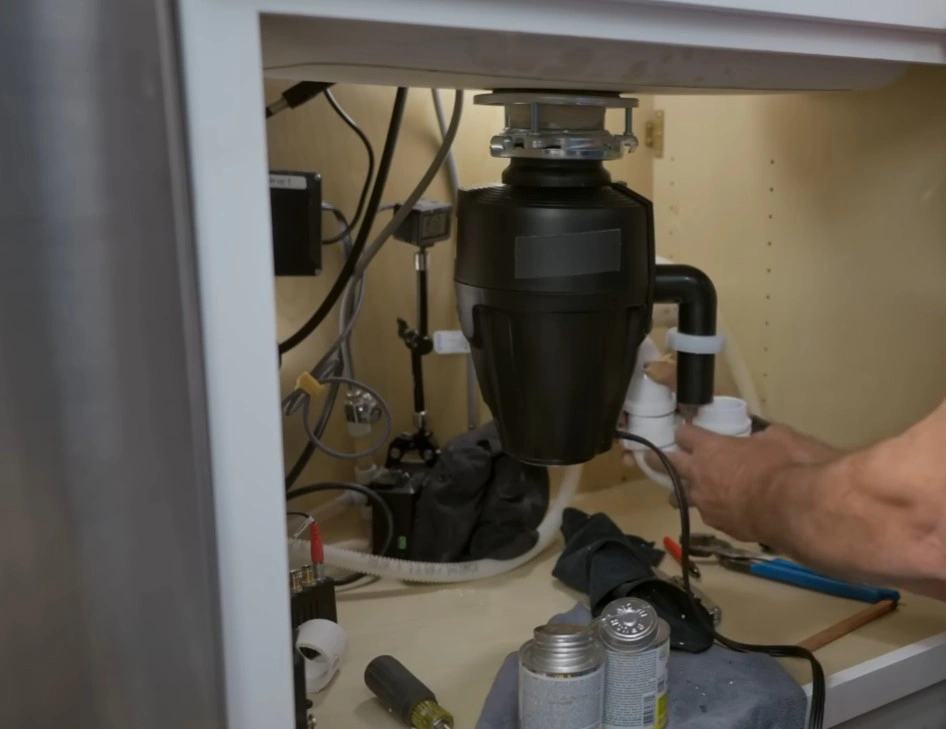 Garbage disposal not working installed under a kitchen sink with plumbing connections and tools visible during troubleshooting