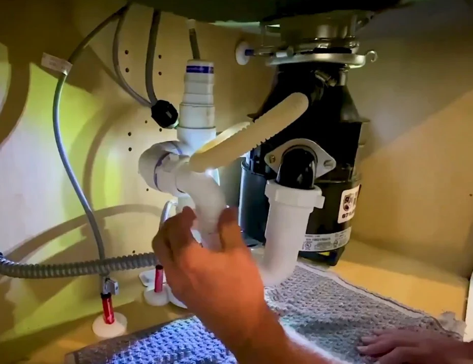 Plumber checking drain pipes connected to a garbage disposal not working under a kitchen sink cabinet